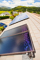 Solar thermal panels for heating hot water with solar PV electric panels behind on a house roof in Ambleside, Lake District, UK. July 2012
