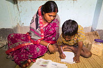 Young boy doing homework in house lit by electricity from battery. Batteries are solar charged from WWF project to supply electricity to a remote island in the Sunderbans, Ganges Delta, India. Decembe...