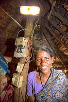 Dalit woman / untouchable woman in her hut, illuminated by an electric light, powered by an A4 sized solar panel, that charges a battery, and enables her to have light. Karnataka, India. December 2013
