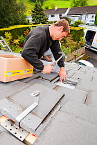 A techinician fitting roof brackets to a house roof in Ambleside, Cumbria, UK, to support solar photo voltaic panels. August 2011