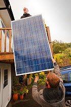 A technician fitting solar photo voltaic panels to a house roof in Ambleside, Cumbria, UK. August 2011
