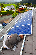 Technicians fitting solar photo voltaic panels to a house roof in Ambleside, Cumbria, UK. August 2011