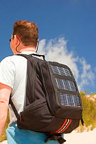Man carrying a solar backpack. The solar panels can be used for recharging mobile phones and other electrical devices. June 2010