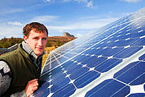 An Eigg crofter and Eigg Electric employee next to their aray of solar PV panels. Isle of Eigg, Scotland, UK. May 2012