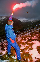 A mountain rescue member uses a flare to attract an approaching sea king helicopter to the casualty site on Fairfield, Lake District, England, UK.