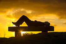 A walker relaxing at sunset,  on Orrest Head above Windermere, Lake District UK. December 2012
