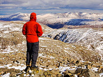 Hill walker on the summit of Scafell Pike  looking towards the Helvellyn Range in the distance.  Lake District, UK, March 2013
