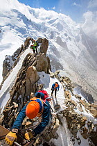 Mont Blanc with climbers on the Cosmiques Arete, climbing the ladder to access the cable car station. Aiguille Du Midi above Chamonix, France, September 2014
