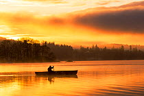 Sunrise over Lake Windermere in Ambleside, Lake District, UK, with a man paddling a Canadian Canoe. December 2014