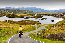 Woman cycling around the Golden road on the East side of the Isle of Harris, Outer Hebrides, Scotland, UK. June 2015