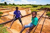 Children playing on tracks of railway bridge swept away by the January 2015 flooding leaving the tracks suspended in mid air, near Bangula. Malawi. March.