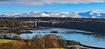 Menai Suspension Bridge, designed by Thomas Telford, viewed from Anglesey across Menai Strait, with snow capped hills in background. North Wales, UK. December 2017
