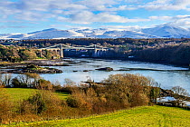 Menai Suspension Bridge, designed by Thomas Telford, viewed from Anglesey across Menai Strait, with snow capped hills in background. North Wales, UK. December 2017.