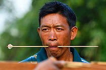 Lisu man holding arrow in mouth during traditional  crossbow competition, Tongbiguan Nature Reserve, Dehong Prefecture, Yunnan province, China, May 2017.