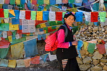 Tibetan woman  in front of Buddhist Prayer flags on the pilgrimage route around Meili Snow Mountain , 6740 m, a Sacred mountain for Tibetan Buddhists,  Yunnan, China, October 2017.