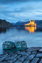 Lobster pots at edge of Loch Duich, Eilean Donan Castle in background. Highlands, Scotland, UK. January 2014.