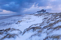 Bamburgh Castle and sand dunes after heavy snowfall, Bamburgh, Northumberland, UK. March 2018.
