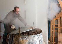 Benoit Dudognon, master paper maker, steaming branches of Paper mulberry (Broussonetia papyrifera) before removing bark. Part of process of making Japanese washi paper. Camargue, France. January.