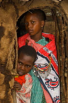 Maasai woman and child peering out hut, Maasai village, Kenya. September 2006.