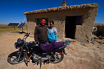 Mongolian shepherd Ge Ri Li Ao De and his wife Ao Te Gen with their motorbike in front of house with solar panels, Inner Mongolia, China. May 2016
