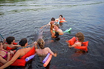 Local fisherman feeding Amazon river dolphin (Inia geoffrensis) surrounded by tourists in the water, Rio Negro, Amazonas, Brazil.