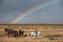 Men on horseback during the round up of mares and foals on marshland, with rainbow.  Donana National Park, Spain. September 2014.