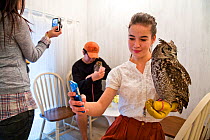 People photographing Spotted eagle owl (Bubo africanus) and taking selfies with mobile phones at the Akiba Fukurou Owl Cafe, Tokyo, Japan.