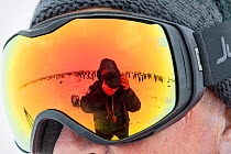 Photographer Sue Flood taking picture of herself and colony of Emperor penguin (Aptenodytes forsteri) in reflection of someone's goggles, Gould Bay, Weddell Sea, Antarctica.
