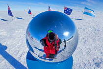 Wildlife photographer Sue Flood reflected in marker at ceremonial South Pole 90 degrees South near Scott-Amundsen base, Antarctica. December 2016