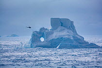 Helicopter from Russian icebreaker Kapitan Khlebnikov flies past iceberg in the Weddell Sea near Snow Hill island emperor penguin colony, Antarctica.