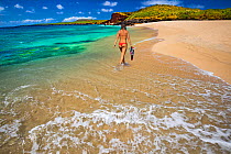 Woman with snorkel equipment walking along water&#39;s edge. Kawakiu Nui Beach, West End, Molokai, Hawaii. July 2017. Model released.