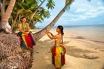 Two girls in traditional costume for cultural ceremonies taking a photo with a smartphone on beach. Yap, Micronesia. September 2013. Model released.