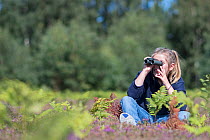 Young girl birdwatching on lowland heath North Norfolk, England, UK. Model released.