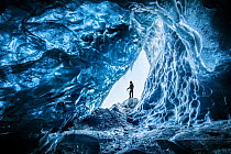 Man at mouth of an ice cave beneath Vatnajokull Glacier, Iceland. March 2018