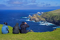 Birdwatchers watching coastline with sea cliffs and stacks, home to breeding seabirds at Hermaness, Unst, Shetland Islands, Scotland, UK, May