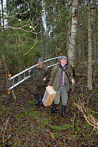 Researchers carrying equipment prior to fitting nest box for Siberian flying squirrel (Pteromys volans). Mature mixed forest, Estonia. April 2018. Model released.
