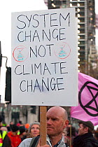 Protestor holding placard &#39;System Change not Climate Change&#39; during Extinction Rebellion demonstration. Five bridges across the Thames were blocked to draw attention to climate change. Westmin...