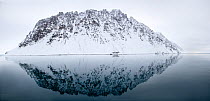 Snow covered mountain reflected in sea. Lillienhookfjorden, Spitsbergen, Svalbard, Norway. April 2018.