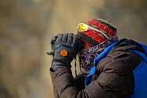 Tracker looking with binoculars for Snow leopard (Panthera uncia) in Spiti valley, Cold Desert Biosphere Reserve, Himalaya mountains, Himachal Pradesh, India, February 2017.