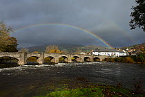 A rainbow over Crickhowell Bridge rebuilt in 1706, Grade 1 listed, the River Usk in spate and Table Mountain in the background, Brecon Beacon National Park, Breconshire, Wales, UK. November 2018.