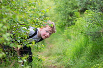 Boy hiding during forest kindergarten session. Aberdeen, Aberdeenshire, Scotland, UK. Editorial use only