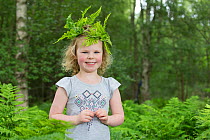 Girl wearing leaf crown during forest kindergarten session, standing amongst ferns. Aberdeen, Aberdeenshire, Scotland, UK. Editorial use only