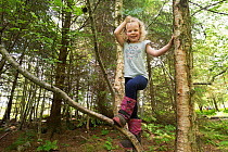 Girl climbing tree in woodland during forest kindergarten session. Aberdeen, Aberdeenshire, Scotland, UK. Editorial use only