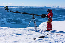 Cameraman Lindsay McCrae using a jib arm filming from ice shelf for BBC Dynasties Penguin programme, Atka Bay, Antarctica. March 2017.