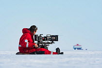 Camerman Lindsay McCrae filming towards Neumayer-Station III, Alfred-Wegener-Institut research station for BBC Dynasties Penguin programme Atka Bay, Antarctica. February 2017.
