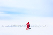 Cameraman Lindsay McCrae filming Emperor penguin (Aptenodytes forsteri) breeding colony on ice shelf in drifting snow, for BBC Dynasties Penguin programme. Atka Bay, Antarctica. October 2017.