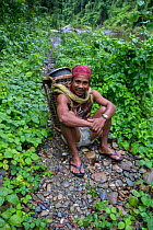 Batak man carrying a traditional rattan backpack resting during an Almaciga tree (Agathis philippinensis) cone collecting expedition in Cleopatra&#39;s Needle Critical Habitat, Palawan, the Philippine...