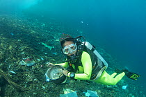 Diver with marine trash underwater, Maluku, Indonesia. November.
