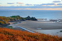 Overview of Three Cliffs Bay at dusk with Pennard Pill stream meandering across the beach to reach the sea at low tide, Penmaen, The Gower peninsula, Wales, UK, October 2018.