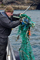 &#39;Ghost Gear&#39;, abandoned fishing net and frayed plastic ropes, found floating in the sea and being hooked out of the water by a member of the Cornwall Seal Group Research Trust to lessen the ri...